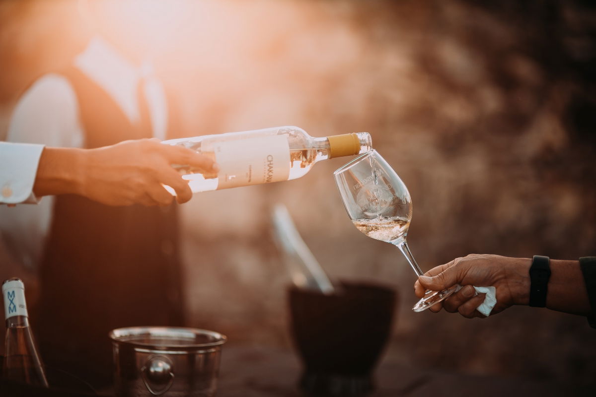 Rose wine being poured from a bottle into a wine glass with the sun in the background.