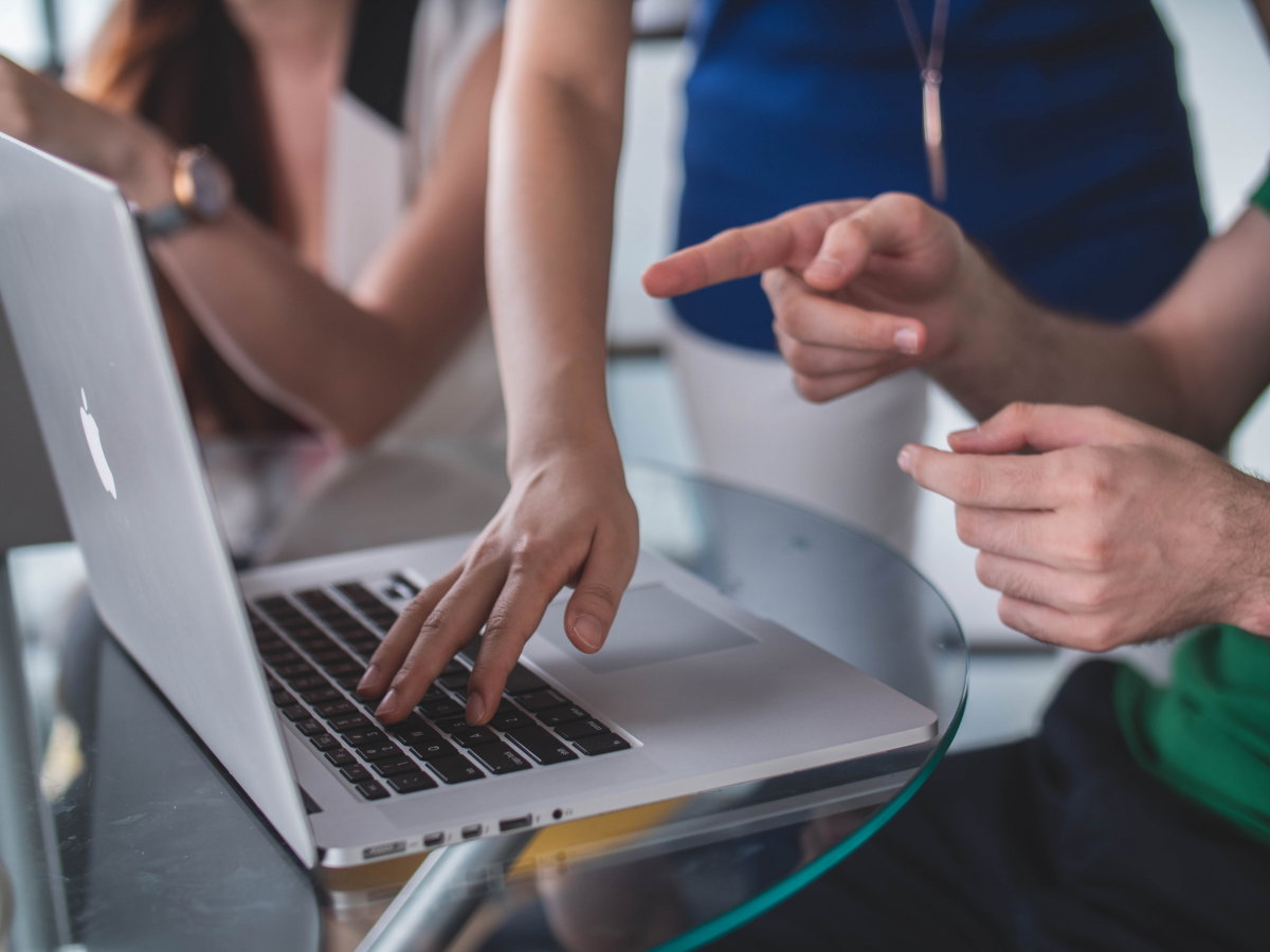 Photo shows someone typing on a Macbook Pro and a colleague pointing to something on the screen.