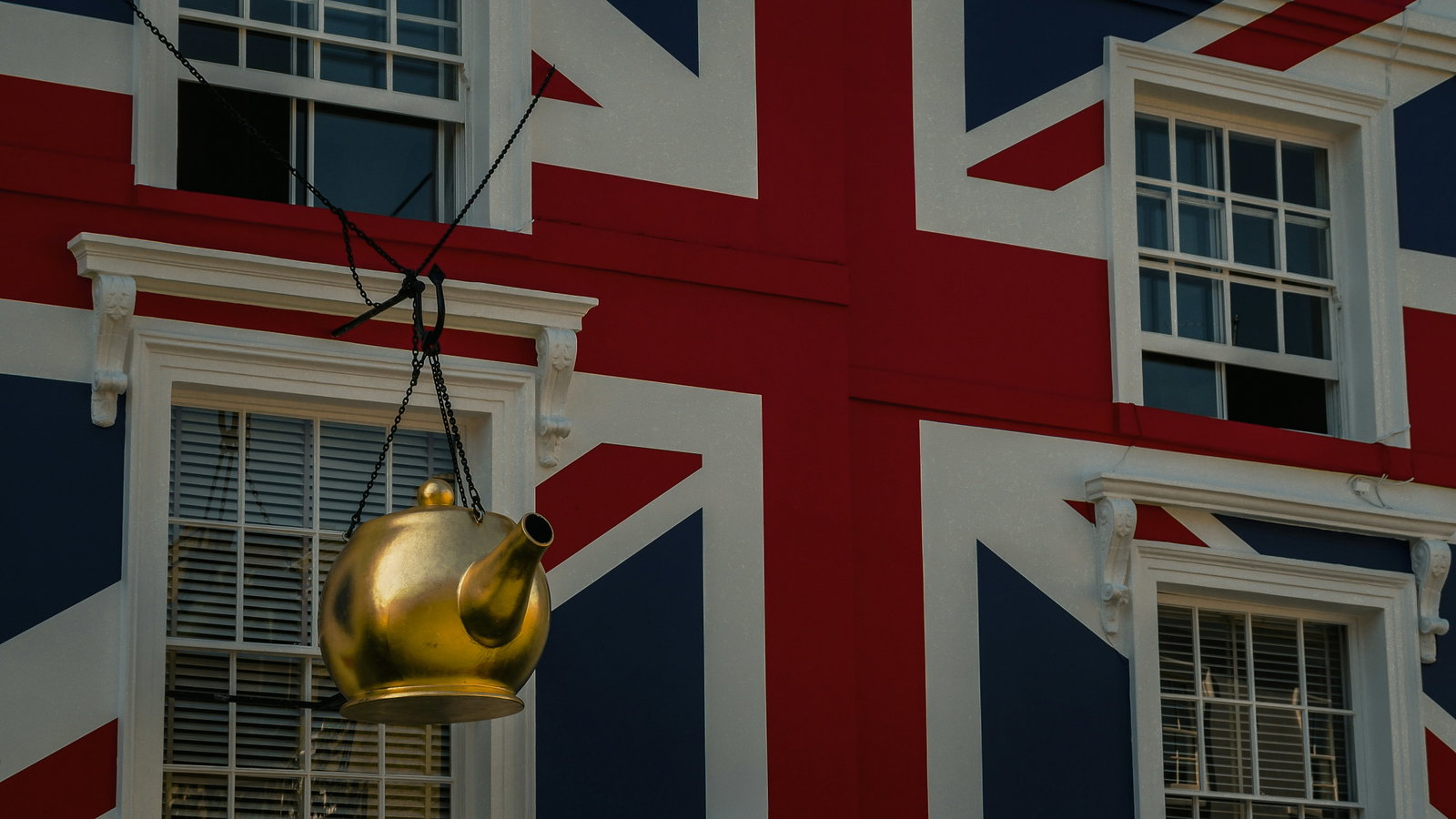 A large gold teapot hanging outside a house in London, painted in the Union Jack